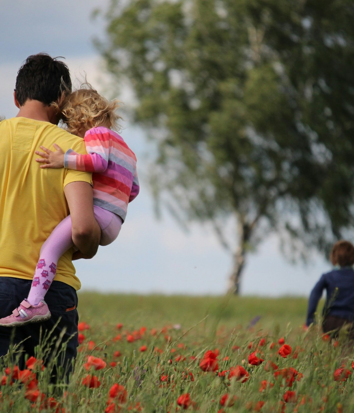 Vater hält Tochter auf dem Arm und beobachtet seinen laufenden Sohn