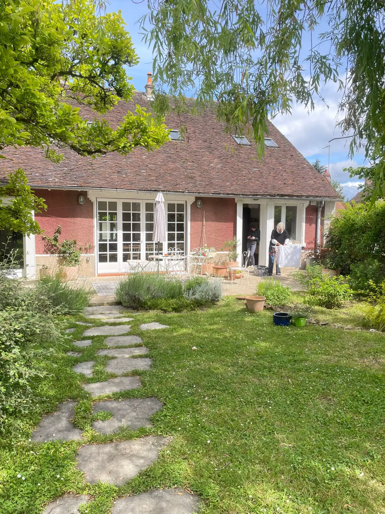Red-render French country house with a terrace and stepping-stone lawn path in spring